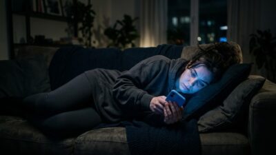 Человек ночью на диване листает смартфон в свете экрана